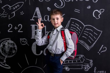 Sevimli öğrenci sırtında Tamam işaret gösteren bir sırt çantası ile bir arka plan olarak kara tahta önce ayakta. Manzara resim
