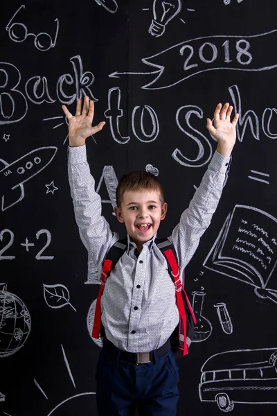 Wesoły i szczęśliwy uczniak stojąc przed chalkboard jako tło z plecakiem na plecach i ręce podniesione. Obraz portret — Zdjęcie stockowe