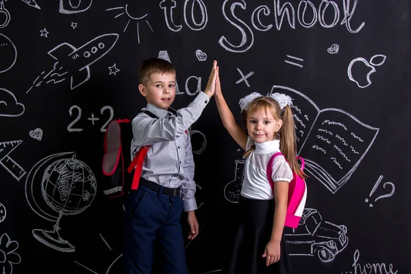 Chłopiec i dziewczynka. Koleżanek, stojąca przed chalkboard jako tło z plecakiem na ich plecach claping ręce patrząc prosto do aparatu — Zdjęcie stockowe