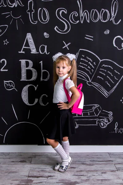 Kokietka uczennica stojący przed chalkboard jako tło z plecakiem na plecach — Zdjęcie stockowe
