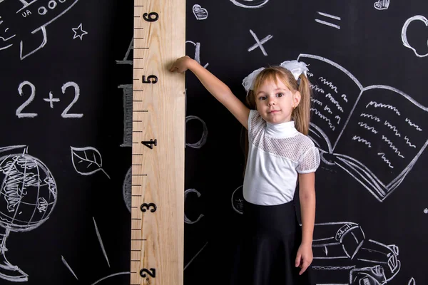 Coquette schoolmeisje staande voor het schoolbord als achtergrond wijzen op de enorme schaal — Stockfoto