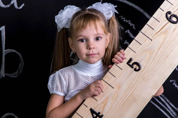 Cute uczennica stojący przed chalkboard jako tło, posiadający ogromny linijki po przekątnej. Powiększony widok — Zdjęcie stockowe