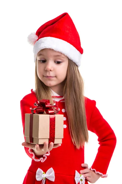 Feliz Natal menina olhando para o presente segurando-o na mão, vestindo um chapéu de Papai Noel isolado sobre um fundo branco — Fotografia de Stock