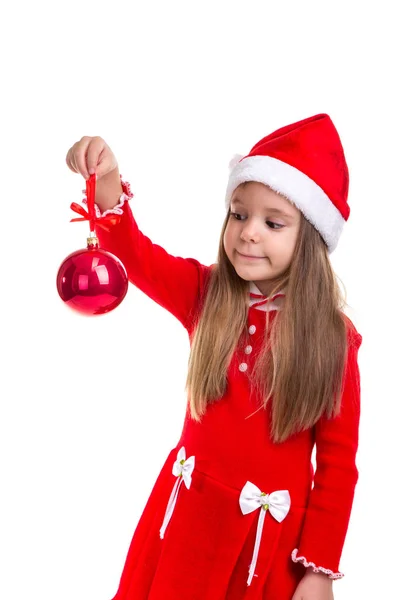 Chica de Navidad sosteniendo y mirando el juguete del árbol de Navidad en la mano, con un sombrero de santa aislado sobre un fondo blanco —  Fotos de Stock