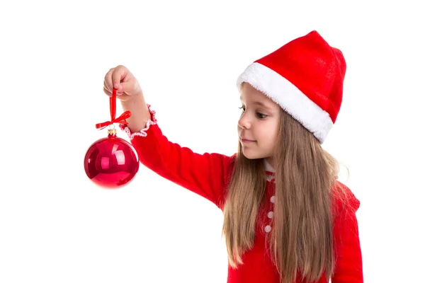 Χριστούγεννα κορίτσι κρατώντας και βλέπουν ένα χριστουγεννιάτικο δέντρο παιχνίδι στο χέρι, φορώντας ένα καπέλο santa απομονωμένη πάνω σε λευκό φόντο, τοπίο — Φωτογραφία Αρχείου