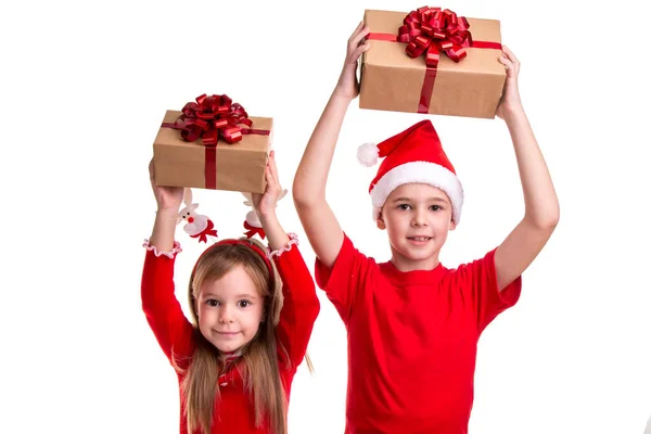 Concepto: Navidad o Feliz Año Nuevo. Niño alegre con sombrero de santa en la cabeza y una chica con cuernos de ciervo, sosteniendo las cajas de regalo sobre sus cabezas —  Fotos de Stock