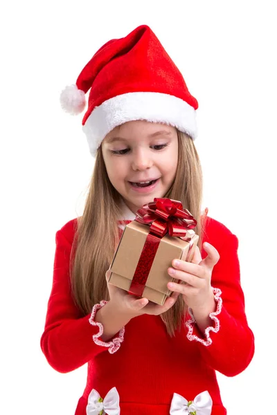 Surpreendida menina natal olhando para o presente segurando-o na mão, vestindo um chapéu de Papai Noel isolado sobre um fundo branco — Fotografia de Stock