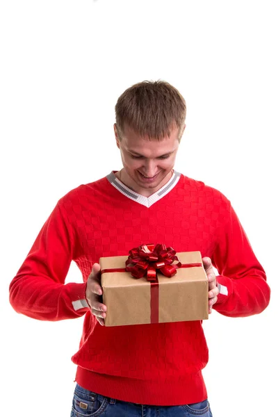 Όμορφος άντρας με το κόκκινο πουλόβερ που βλέπουν σε ένα κιβώτιο δώρων στα χέρια του, απομονωθεί σε λευκό φόντο. Γιορτή έννοια — Φωτογραφία Αρχείου