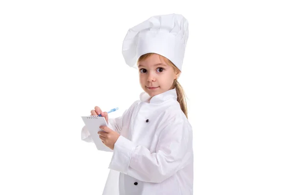 Adorável menina chef uniforme branco isolado no fundo branco. Escrevendo as notas, olhando diretamente para a câmera. Paisagem — Fotografia de Stock