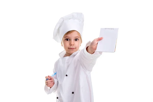Щаслива дівчина шеф-кухаря білої форми ізольована на білому тлі. Тримаючи і показуючи порожню ноту, дивлячись на камеру і ручку з іншого боку. Ландшафтний образ — стокове фото