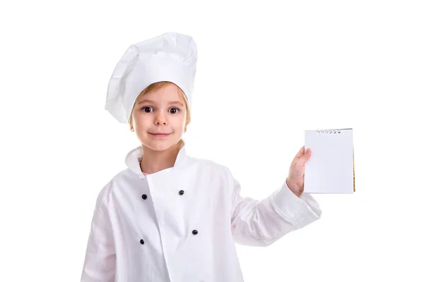 Uśmiechnięta dziewczyna kucharzem biały uniform izolowana na białym tle. Gospodarstwa i pokazuje puste notatki, patrząc na kamery — Zdjęcie stockowe