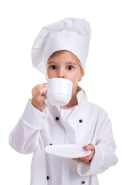 Menina feliz chef uniforme branco isolado no fundo branco. Beber da taça branca segurando um pires. Imagem do retrato — Fotografia de Stock