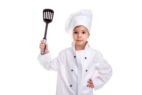 Girl chef white uniform isolated on white background. Holding black scapula up with another hand on the waist. Looking at the camera. Landscape image — Stock Photo, Image