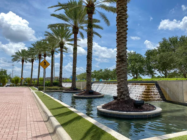 An outdoor view of a water feature at a mall with a line of palm trees beside it.