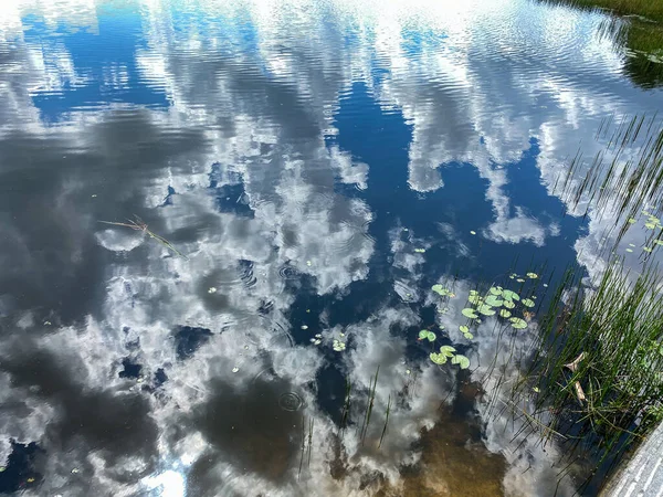 The clouds in the sky reflecting on a calm peaceful lake on a beautiful summer day.