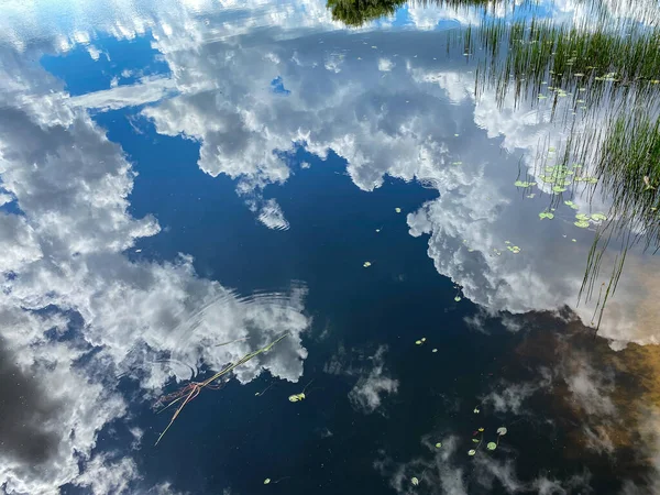 The clouds in the sky reflecting on a calm peaceful lake on a beautiful summer day.
