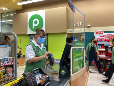 Orlando, FL / USA-7 / 23 / 20: Yüz maskesi ve pleksiglas kalkan takan bir Publix market çalışanı Orlando, Florida 'daki bir müşteriyi kontrol ediyor.