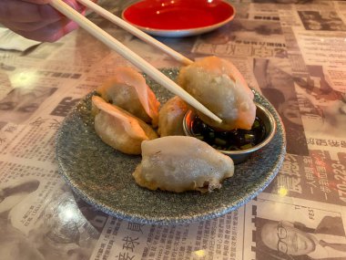 Asya füzyon restoranındaki soslu küçük bir konteynıra çubuk kullanarak tavuk köftesi batıran bir adam..