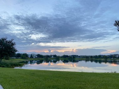 Güzel pembe, turuncu ve mavi gün batımı bir banliyö gölünde yansıyor..