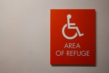 Bir apartmanın koridorunda üzerinde tekerlekli sandalye sembolü olan Sığınak Alanının engelliler için acil toplanma yeri olduğu yazan bir tabela..