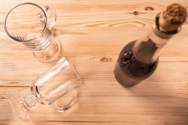 Diferansiyel odaklanma. İçi boş şeffaf bardaklar, bacağında sıcak şarap ve kırmızı şarap şişesi var. Yapılandırılmamış, parlak bir ahşap tahta üzerinde, yukarıdan yakın görüş..