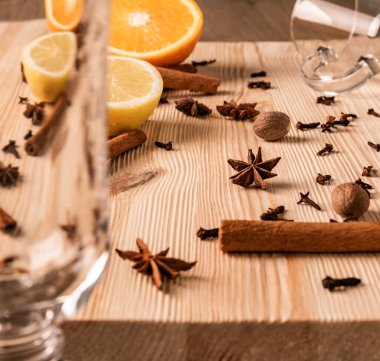 Diferansiyel odaklanma. Şeffaf boş bardaklar şarap, anason çiçekleri yıldızlar, hindistan cevizleri, karanfiller, mis kokulu tarçın çubukları, limon ve turuncu yapılandırılmış doğal ahşap tahtada, yakın görünüm.