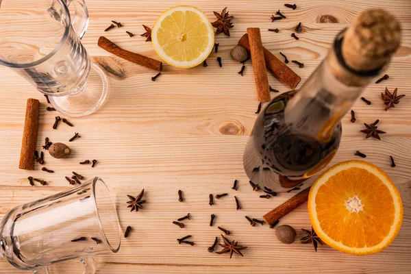 Differential focus. Limpid glasses for mulled wine, cork bottle with red wine, anise flowers, cloves, fragrant cinnamon sticks, lemon and orange on structured natural wooden board, close up above view