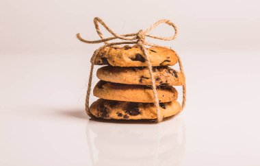 Siyah çikolata sargılı dört kum bisküvisi, parlak beyaz plastik bir zemin üzerinde, yansımalarını gösteriyor. Üstü yay ile bağlanmış..