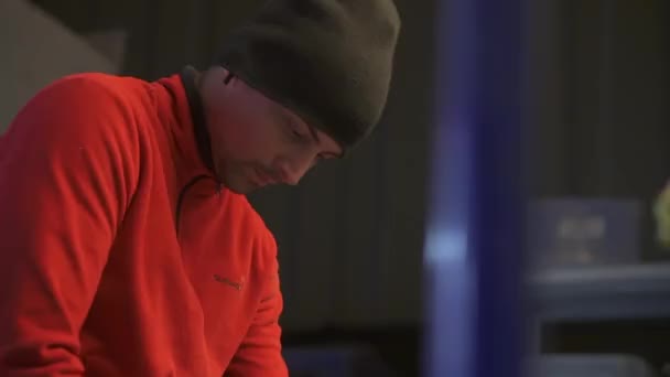 Pria kaukasia dengan pakaian merah dan topi hitam di bengkel sibuk dengan proses kerja — Stok Video