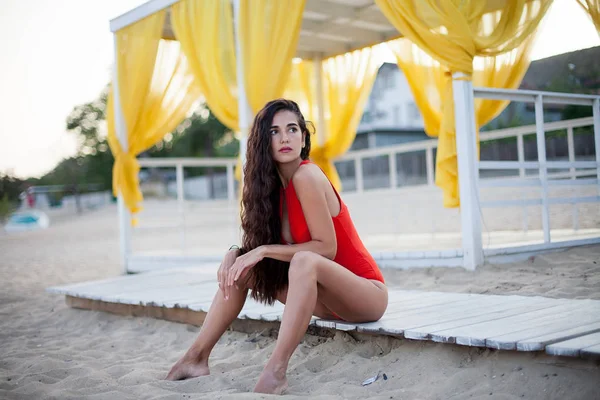 Young beautiful woman in red bikini with long curly hair posing and enjoing her life in seaside. Perfect hair and skin, red lips, stylish makeup.