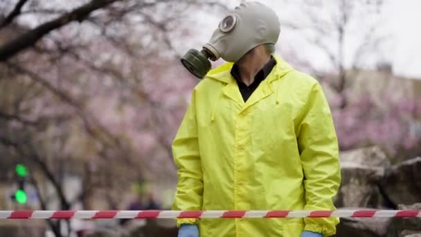 Un hombre con una máscara de gas se para frente a una cinta protectora en la calle — Vídeos de Stock