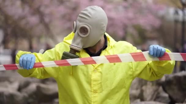 Egy férfi sárga kabátban gázálarcban hozzáér a védőszalaghoz kesztyűben. — Stock videók