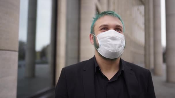 Мужчина с окрашенными волосами стоит в маске на улице и улыбается — стоковое видео