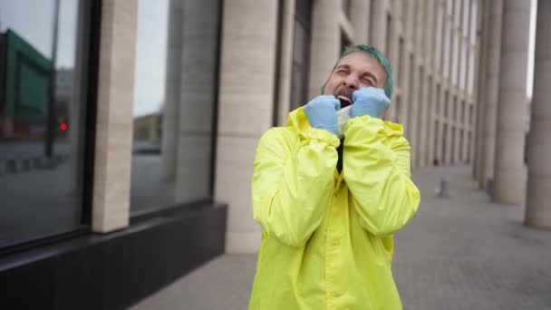 Mann in gelber Jacke zieht wütend medizinische Maske aus dem Gesicht — Stockvideo