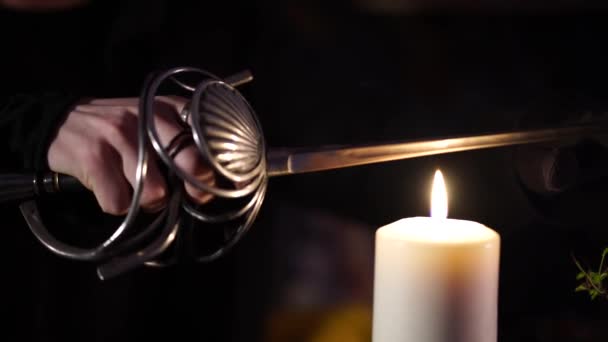 Sword glows over the flame of a wax candle — Stock Video