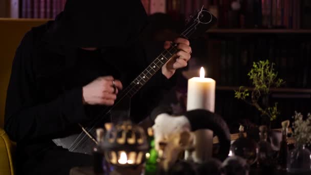 Černý kouzelník hraje na černé balalejce při svitu svíčky — Stock video