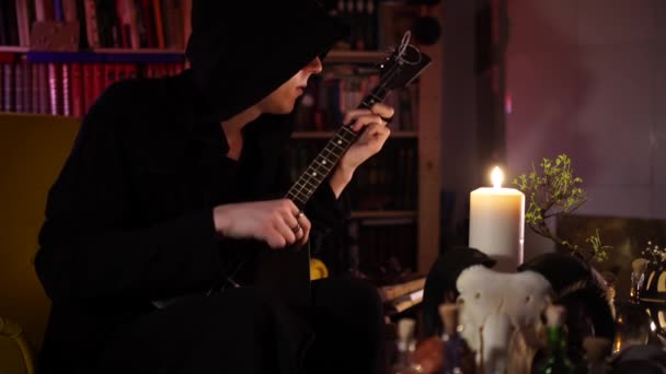 Penyihir hitam memainkan balalaika hitam dengan cahaya lilin — Stok Video