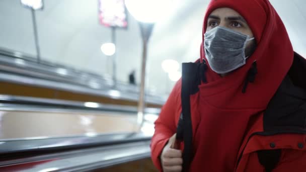 Mężczyzna o wyglądzie kaukaskim w masce ochronnej jeździ po ruchomych schodach metra — Wideo stockowe