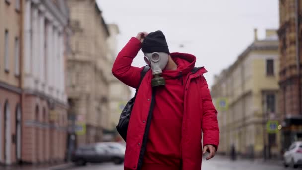 Um homem de vermelho tira o chapéu e a máscara de gás numa rua da cidade — Vídeo de Stock
