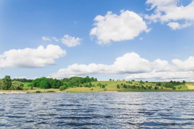 Tepenin arkasında ağaçlarla kaplı bir nehir ve tepesinde büyük, güzel bulutlar...