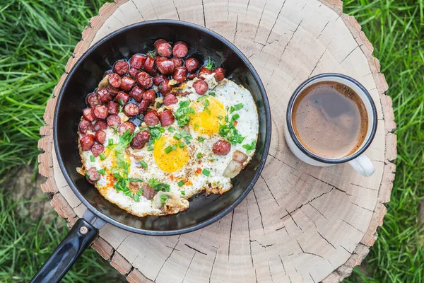 breakfast in nature: scrambled eggs with sausage and coffee on a stump in the forest