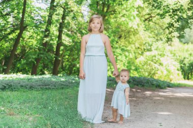 Benzer mavi elbiseli iki kız kardeş parkta yürüyor.