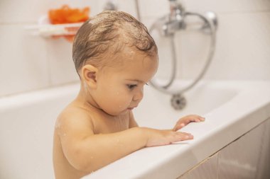 Kafasında şampuan olan şirin bir bebek banyoda banyo yapıyor.