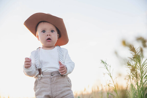baby in a suit with suspenders standing in a field with wheat