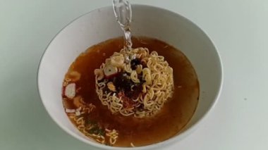 Ağır çekim Pour sıcak suyun içine bir anlık erişte beyaz kase ve fastfood ve sağlıksız yiyecek ya da şişman kavramı olduğunu