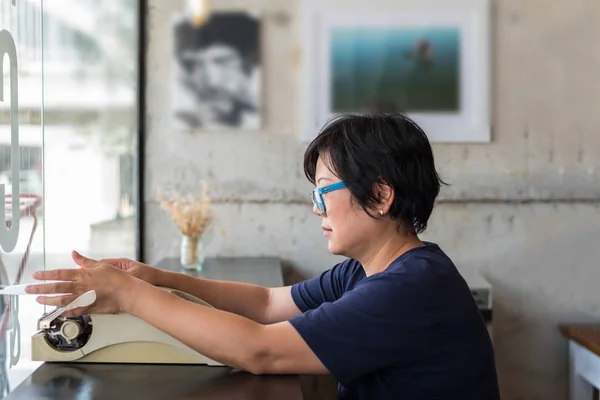 Asian woman 40s white skin with eyeglass sitting for writing something by vintage typewriter in a coffee shop cafe