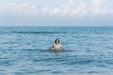 Mutlu kıvırcık saçlı Asyalı yaşlı kadın 60'ların seyahat ve denizde sakin ol ve ne zaman plaj tatil seyahat relax için