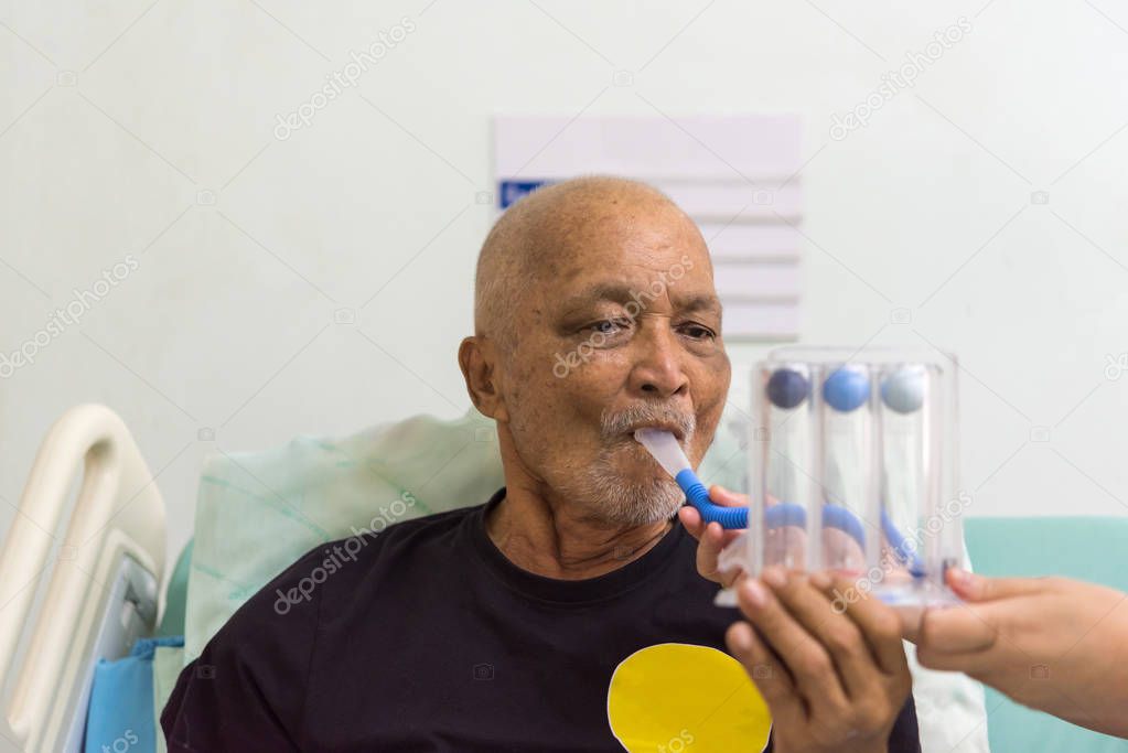 Patient asian elder man 70s use Incentive Spirometer or Triball Tri Flow Meter is medical device to help patients improve the functioning of their lungs on patient bed in ICU. room at hospital.
