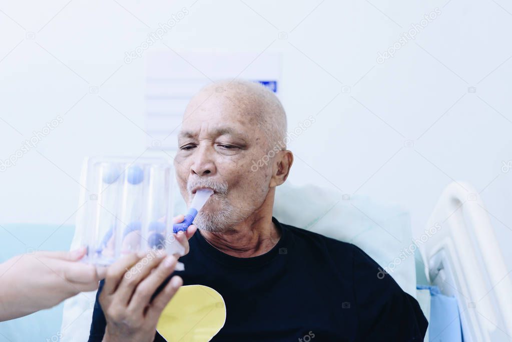 Patient asian elder man 70s use Incentive Spirometer or Triball Tri Flow Meter is medical device to help patients improve the functioning of their lungs on patient bed in ICU. room at hospital.