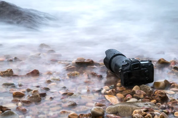 DSLR camera on stone beach wet from water sea wave — Stock Photo, Image